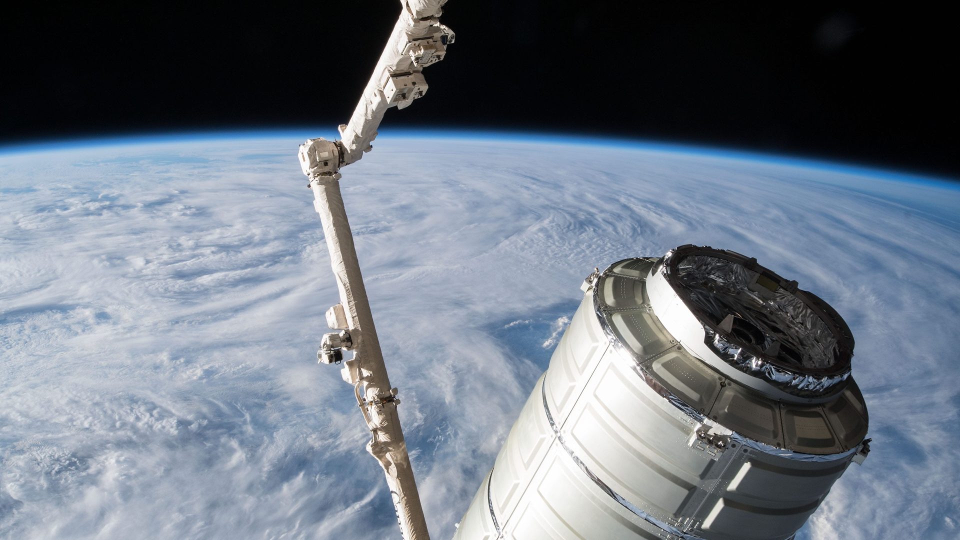 The Orbital ATK space freighter is slowly maneuvered by the Canadarm2 robotic arm scaled